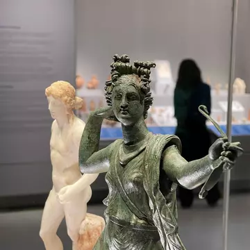 Two sculptures – one in bronze, one in white marble – depicting ancient gods are on display in a museum.
