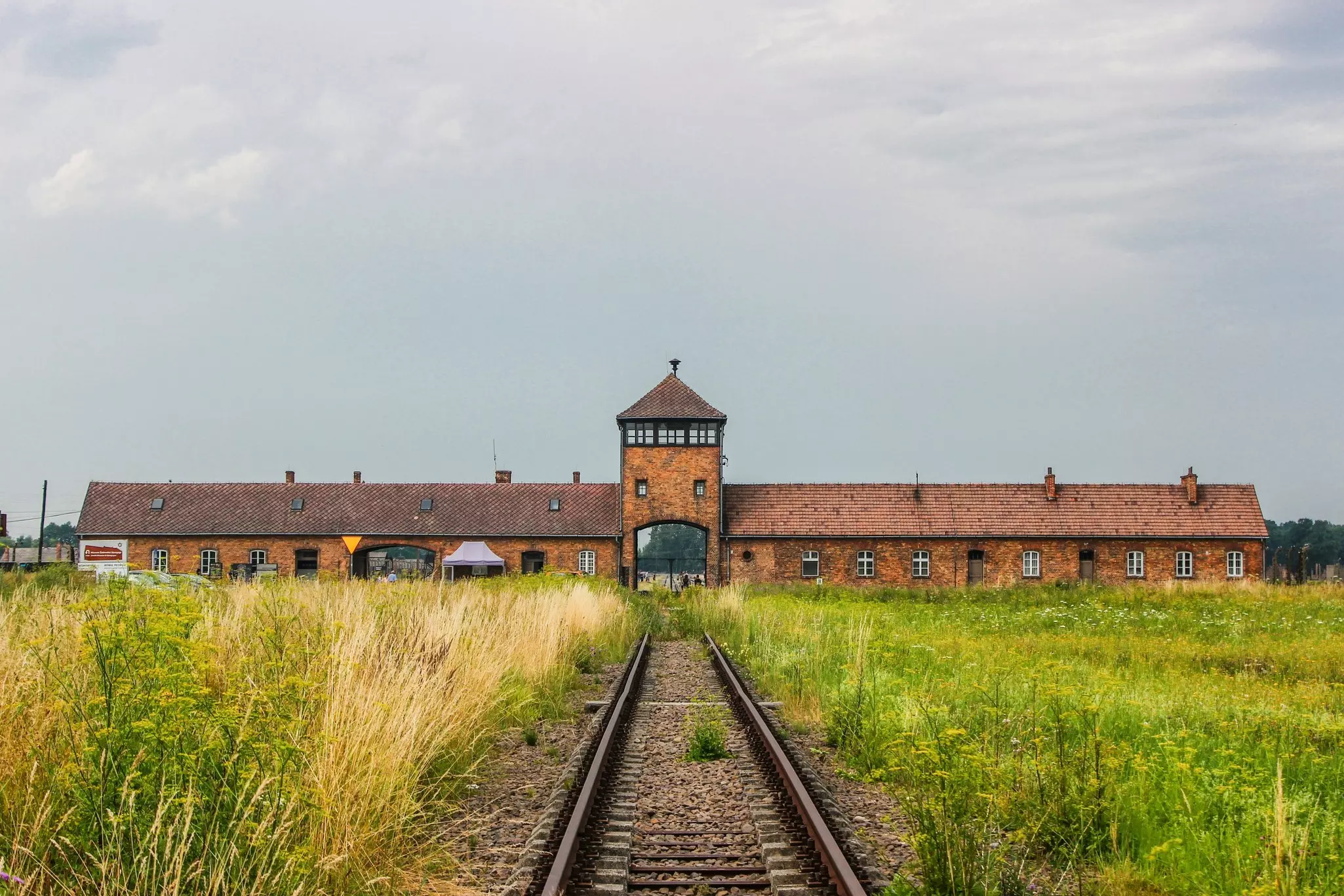 Train tracks cut through grass leading to the red brick Auschwitz-Birkenau Memorial and Museum in Poland.
