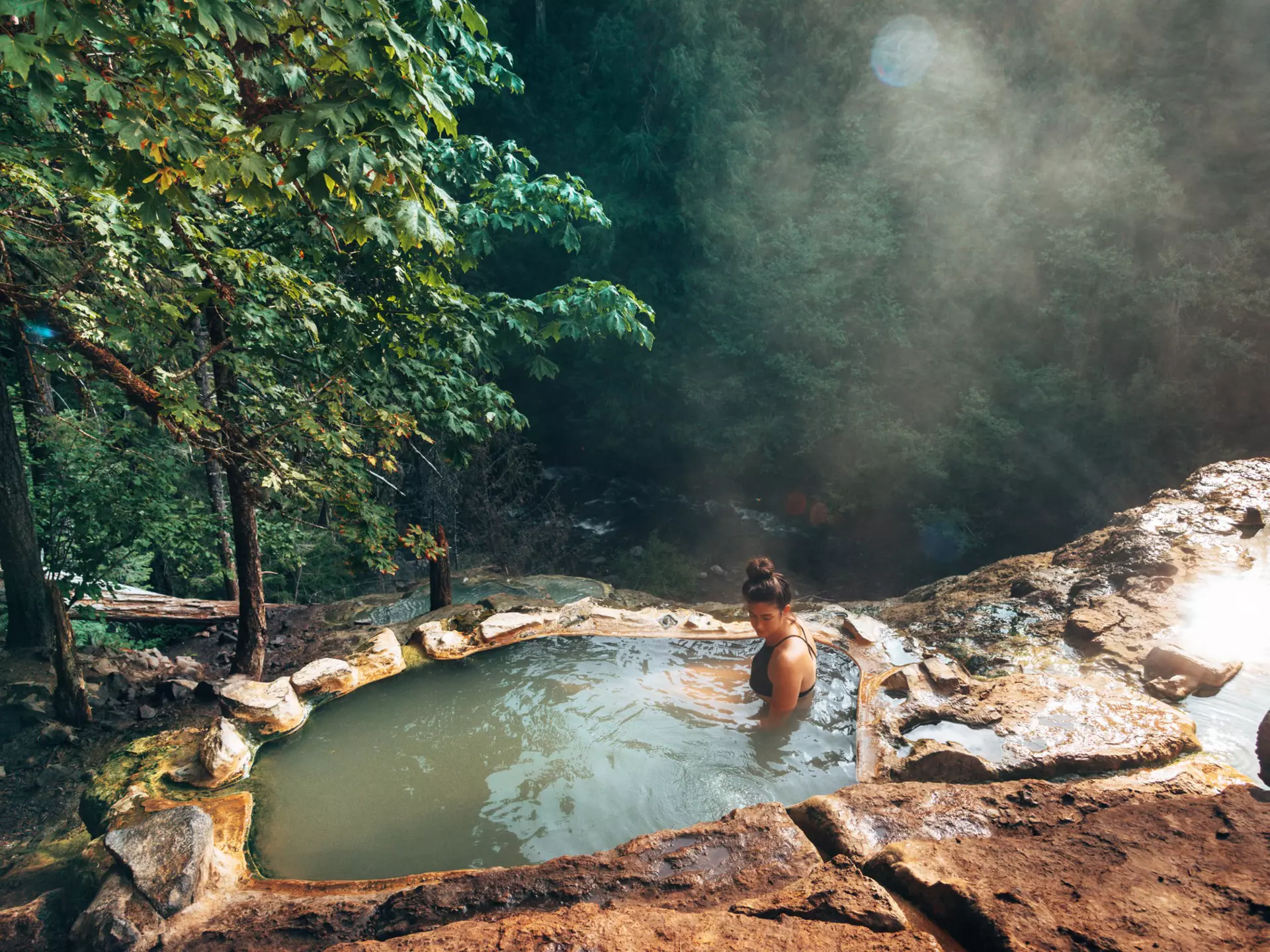 A woman in a hot spring surrounded by forest. 