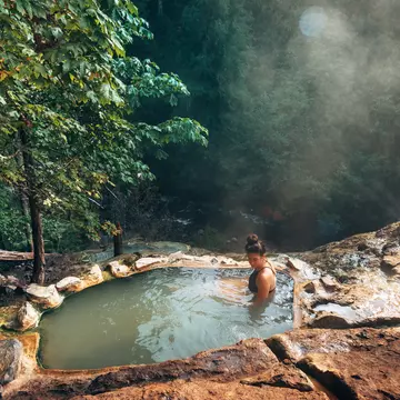 A woman in a hot spring surrounded by forest. 