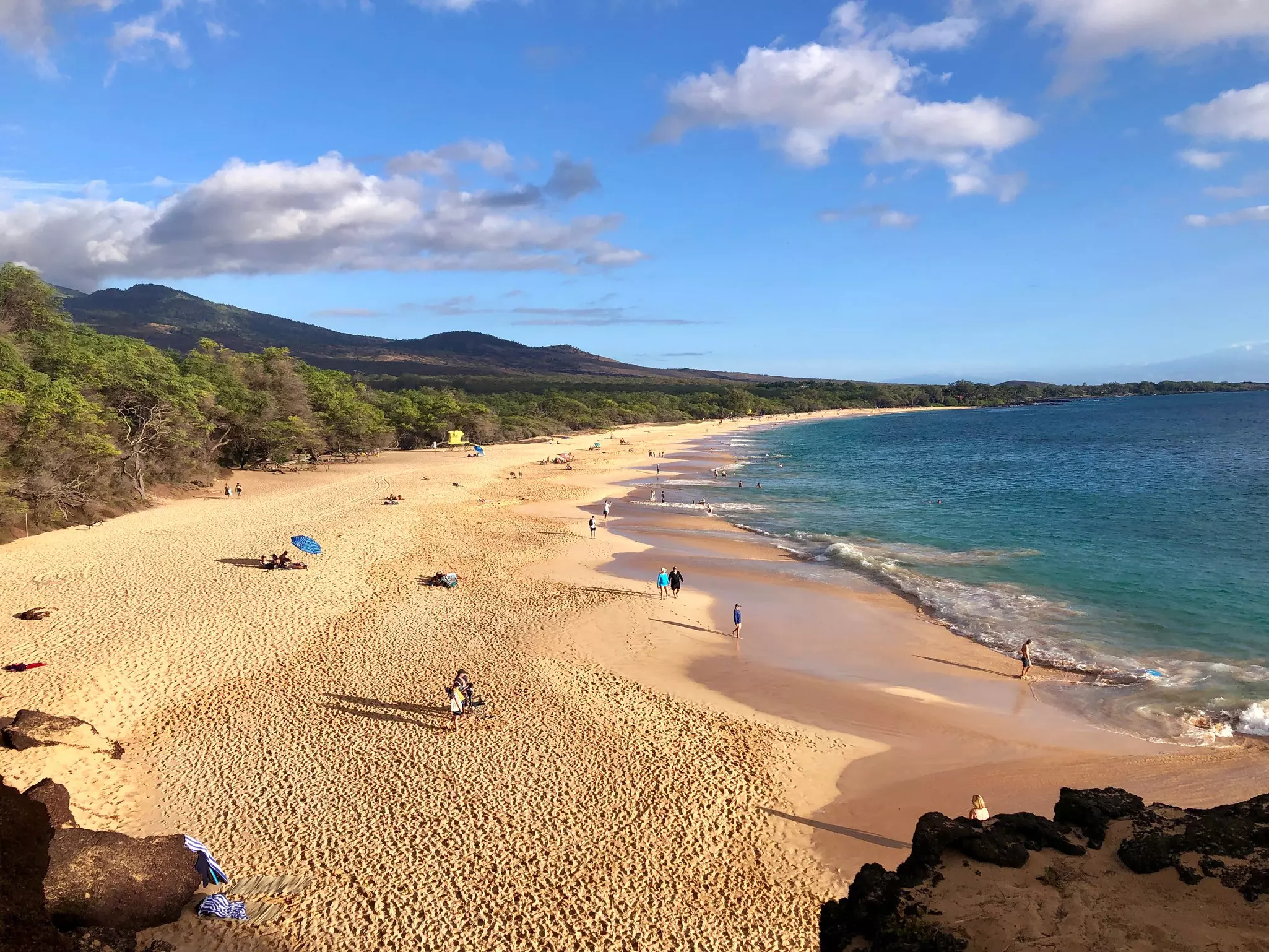 Beachgoers are very spread out on a long strip of golden, crescent-shaped sand