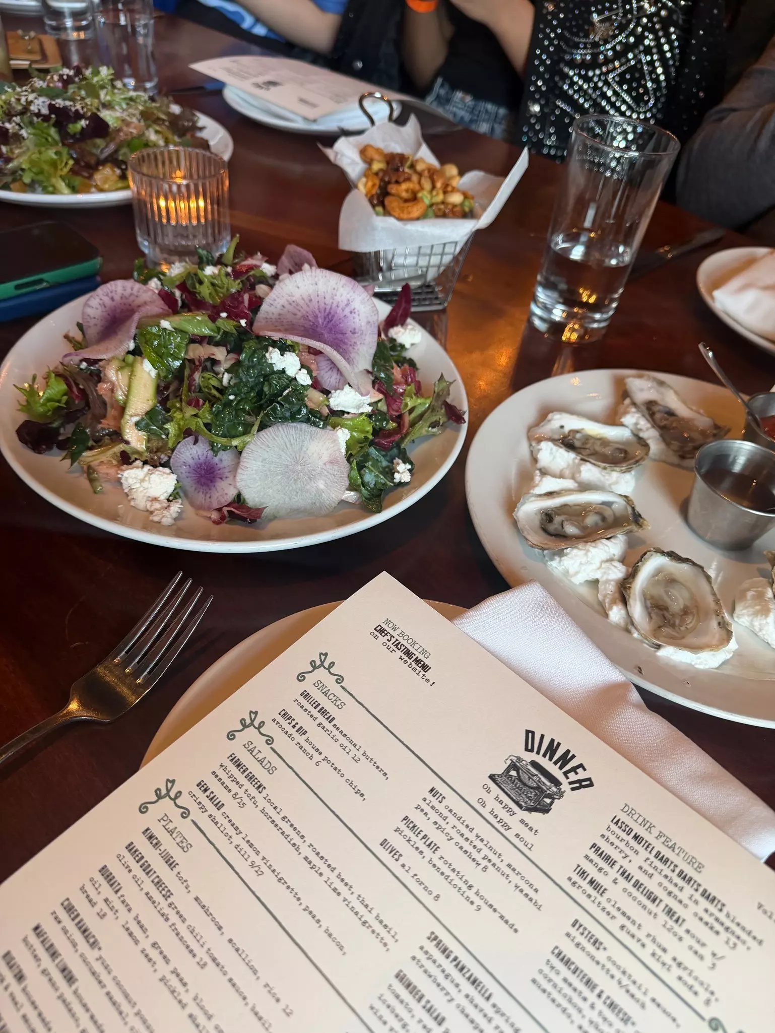 Closeup of a menu, a plate of salad and oysters on a large wooden table at a restaurant