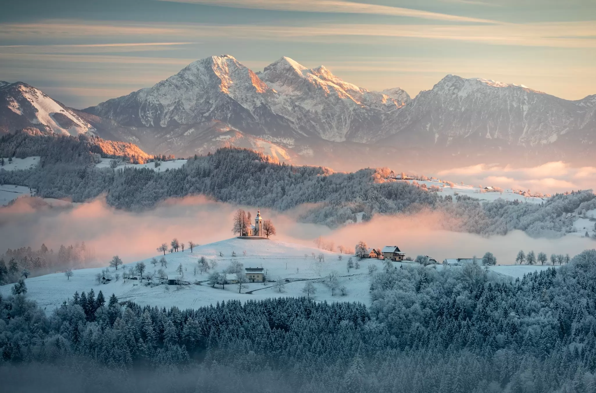 A foggy sunrise in a snowy countryside with a church on a hill.