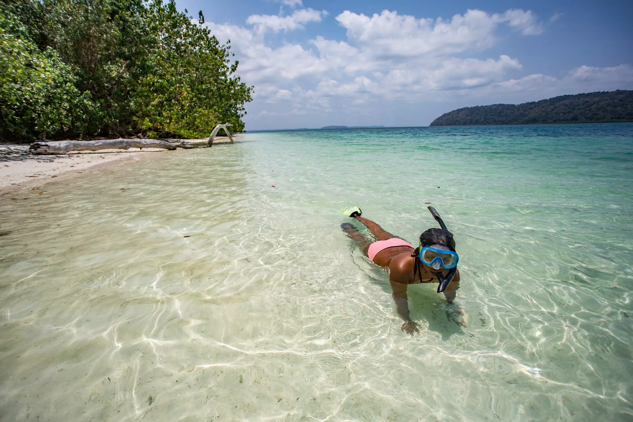 A girl with mask and snorkel swims in shallow clear waters just off a beach