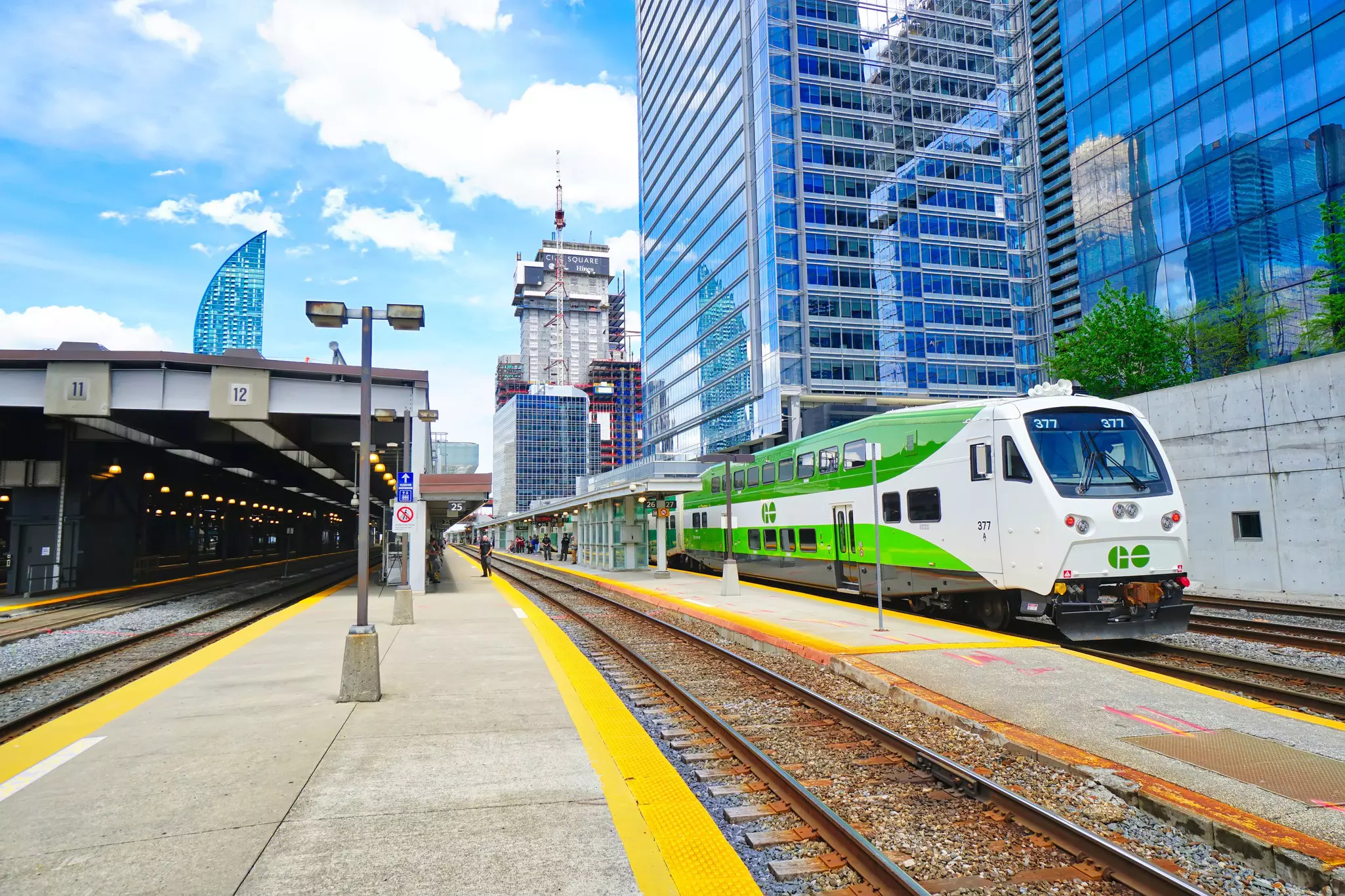 A train with double-decker carriages sits at the platform of a train station surrounded by the office towers of a major city.