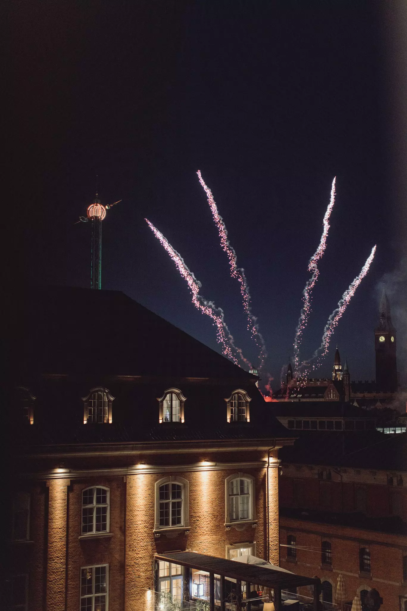 Fireworks shoot into a night sky with an old brick building in the foreground