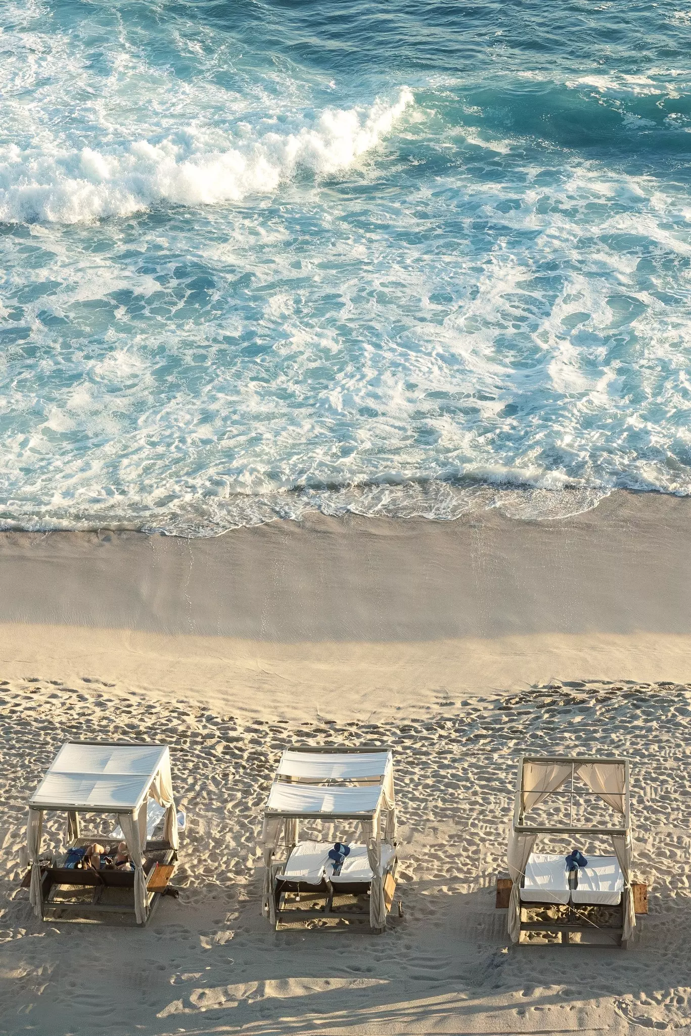 Person Sunbathing at Luxurious Beachfront Cabanas Overlooking Ocean Waves in Cabo San Lucas.