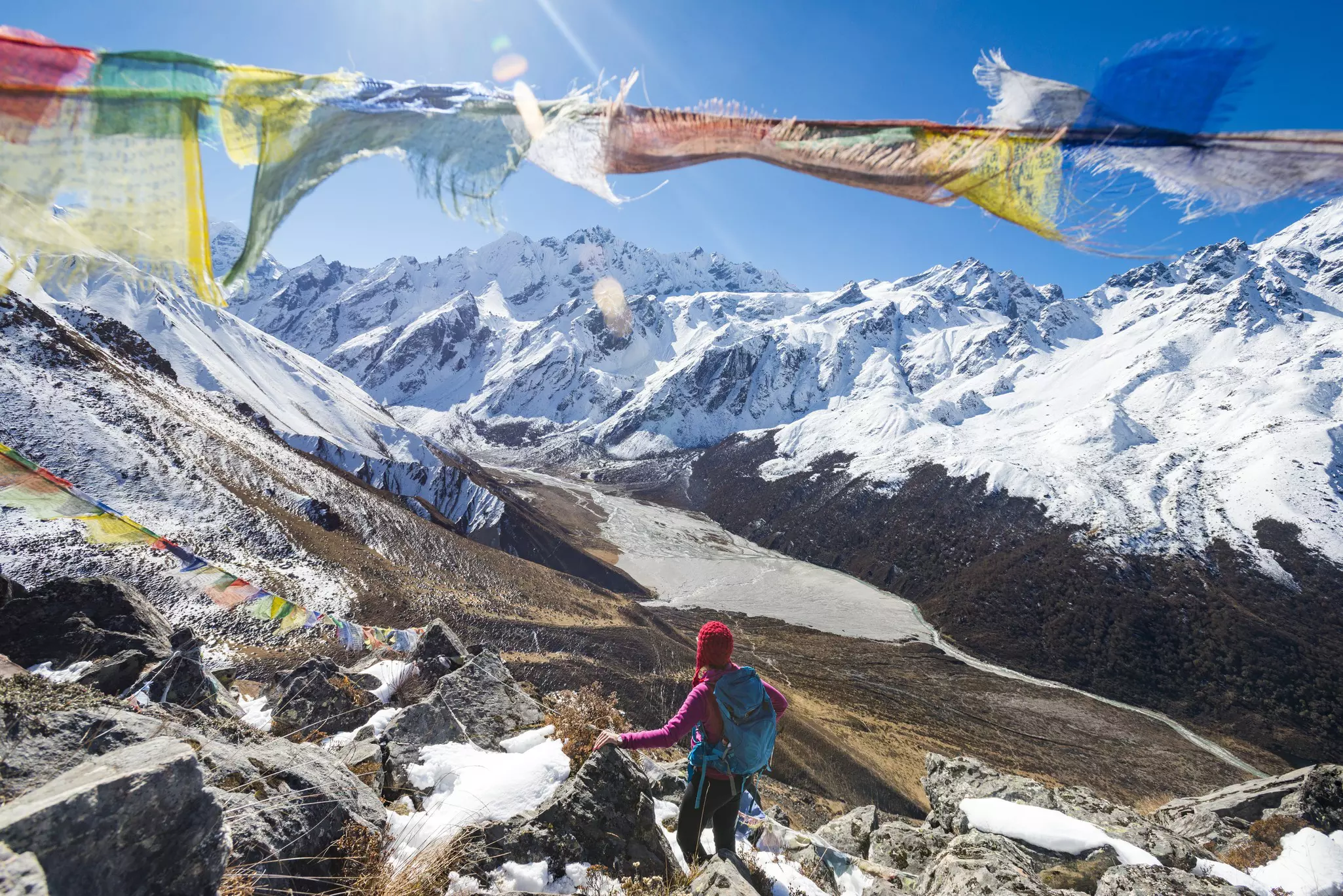 A woman trekking in the Langtang valley in Nepal stands on the top of Kyanjin Ri among prayer flags and looks out towards Ganchempo in the distance