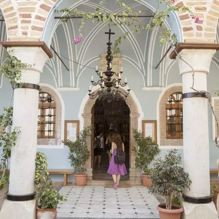 A woman walks into the door of a light blue, ornately designed church. 
