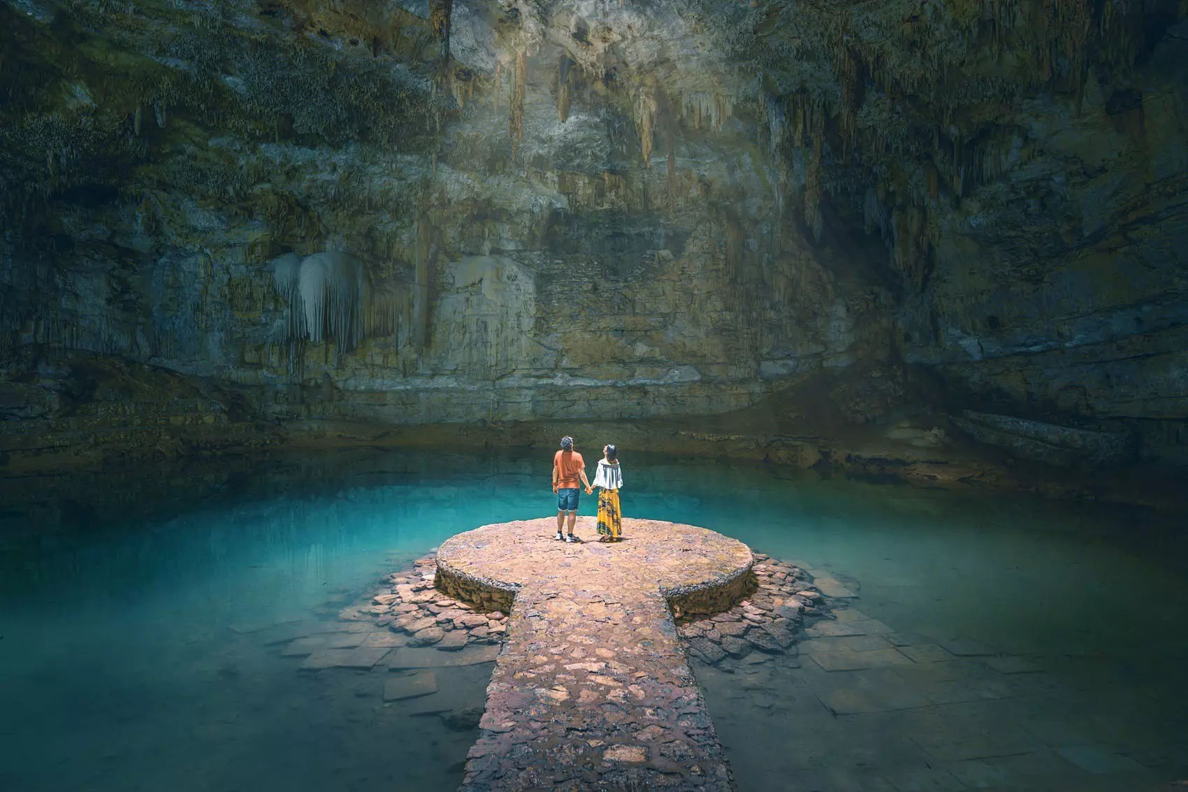A couple hold hands in a sunlit cavern in Yucatan