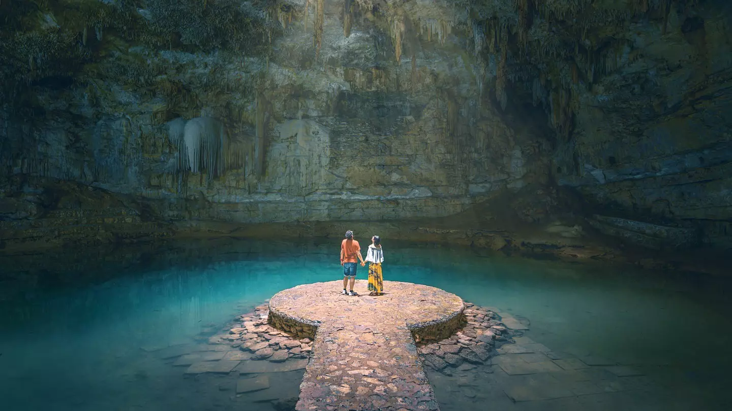 A couple hold hands in a sunlit cavern in Yucatan