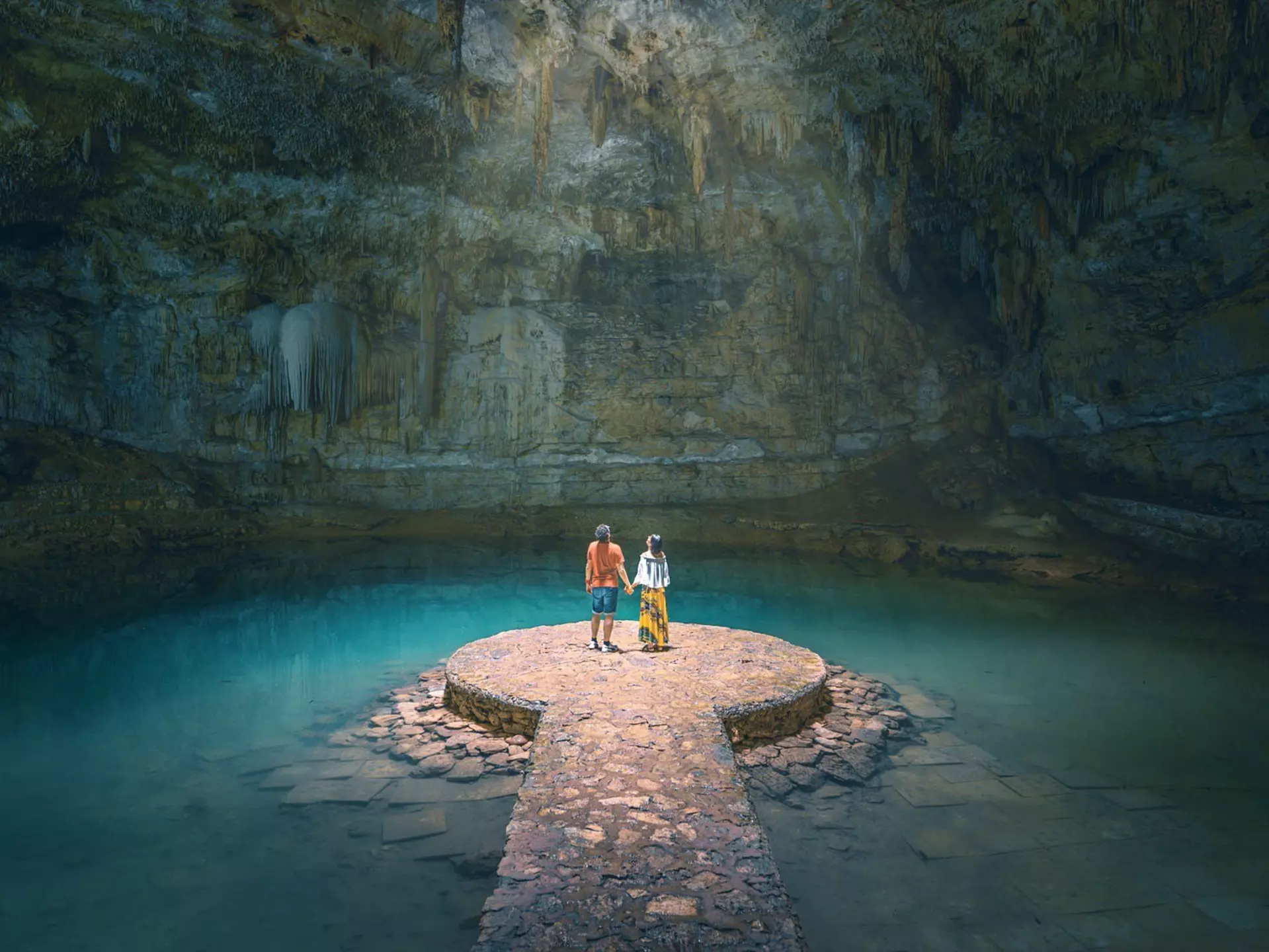 A couple hold hands in a sunlit cavern in Yucatan