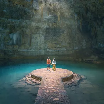 A couple hold hands in a sunlit cavern in Yucatan