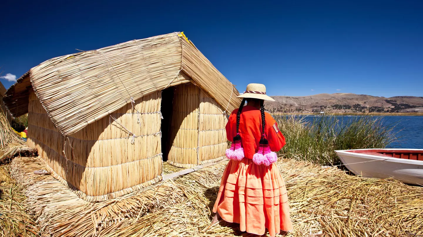A woman stands outside a reed house on Lake Titikaka, Peru.