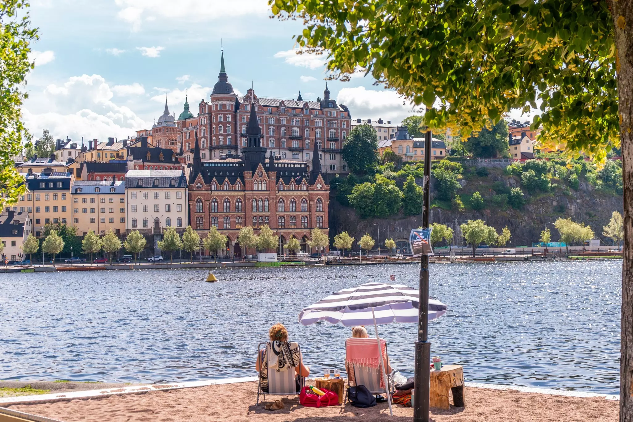 People enjoying the summer sun on a sand bed infront of historical buildings of Södermalm.