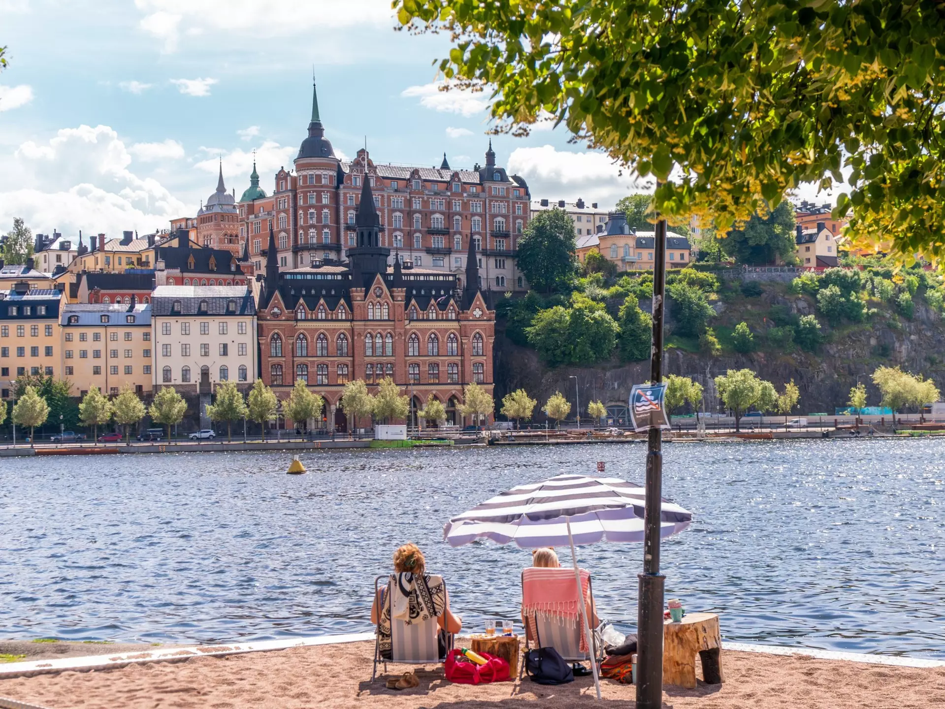 People enjoying the summer sun on a sand bed infront of historical buildings of Södermalm.
