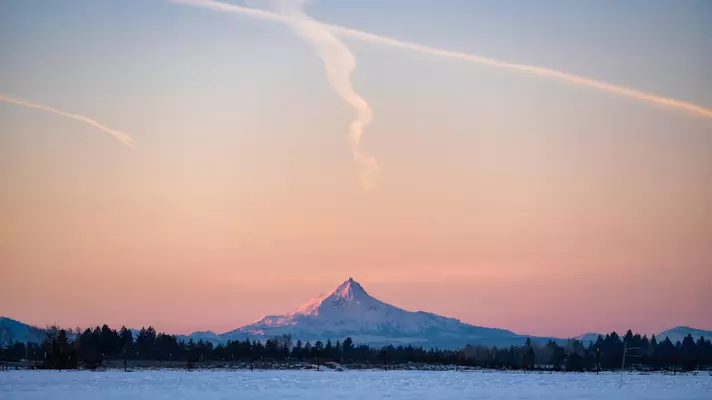 A field in the winter at sunset with a distant mountain peak
