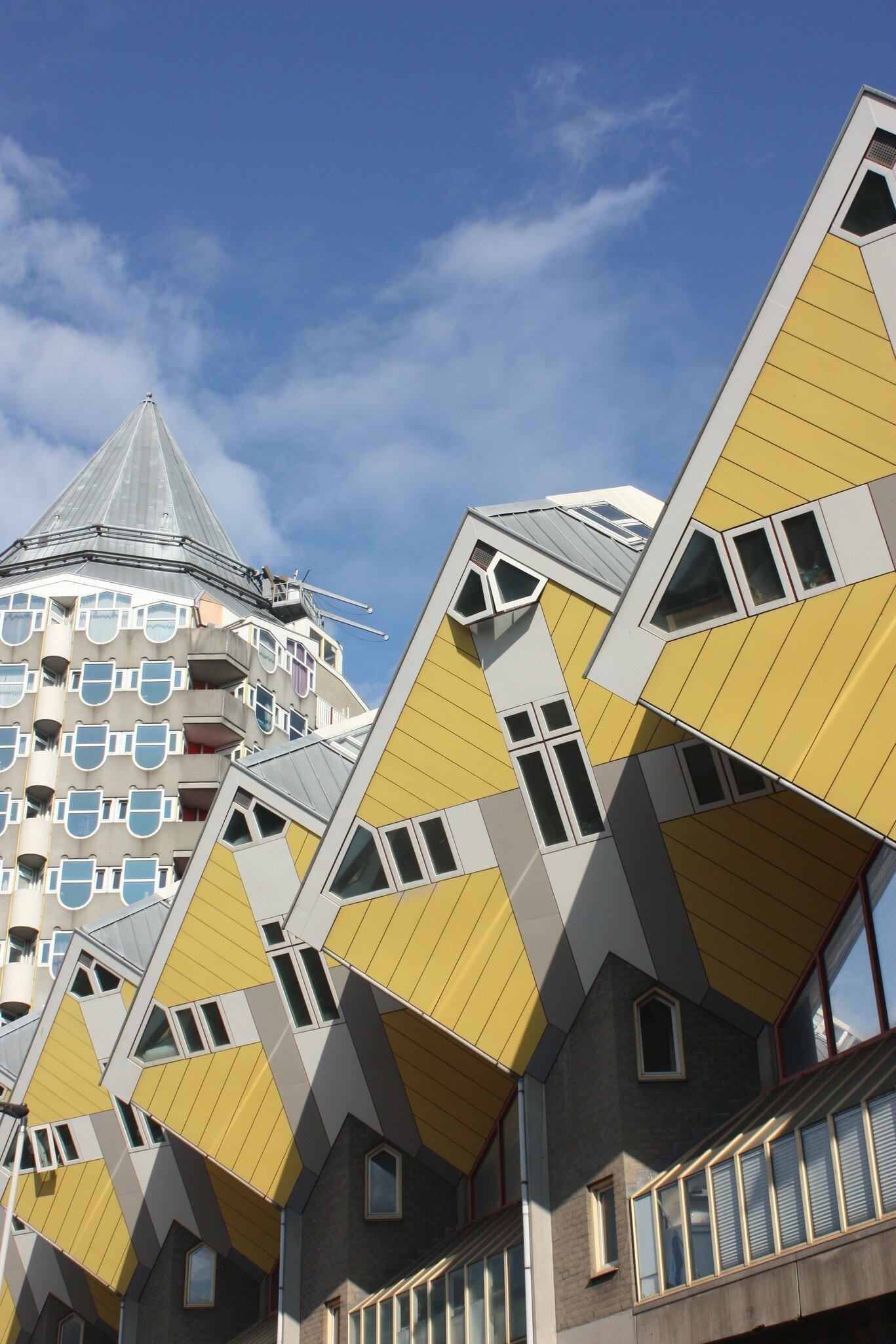 Angled yellow-and-grey cube-shaped apartments with small windows under a blue sky, a pointed tower block behind