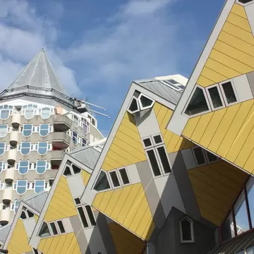 Angled yellow-and-grey cube-shaped apartments with small windows under a blue sky, a pointed tower block behind