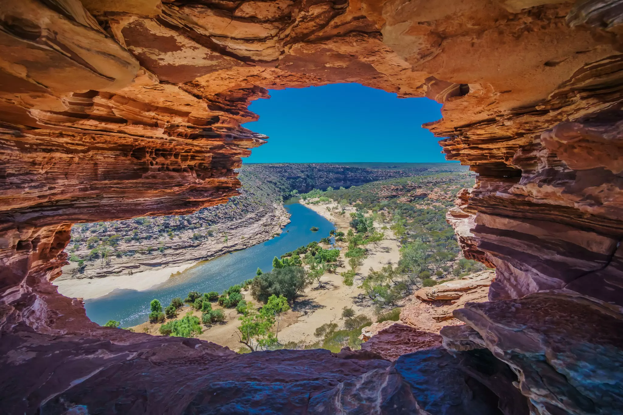 A river runs through a gorge surrounded with dramatic red-rock formations.