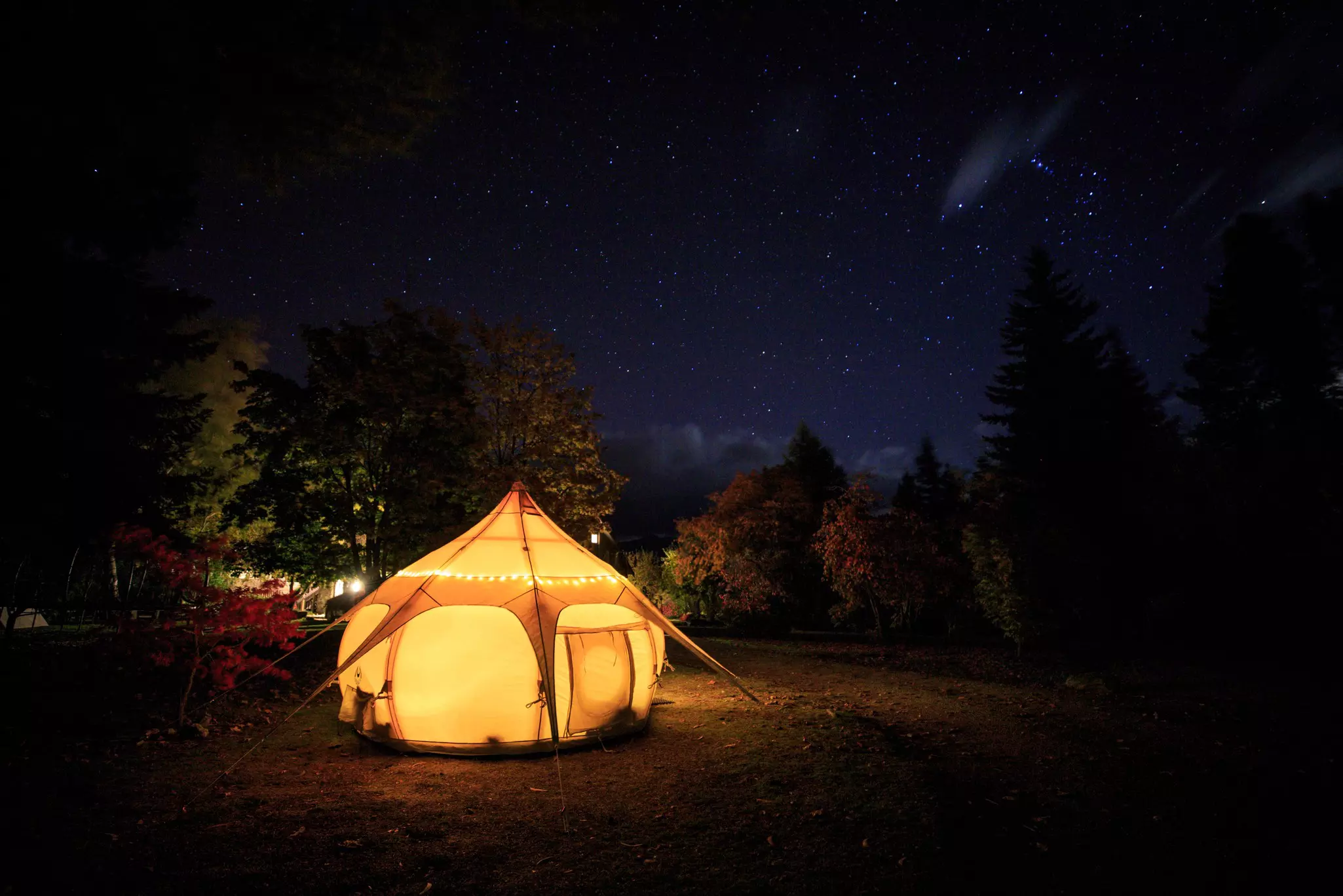 A bell tent lit up in yellow light under a night sky.