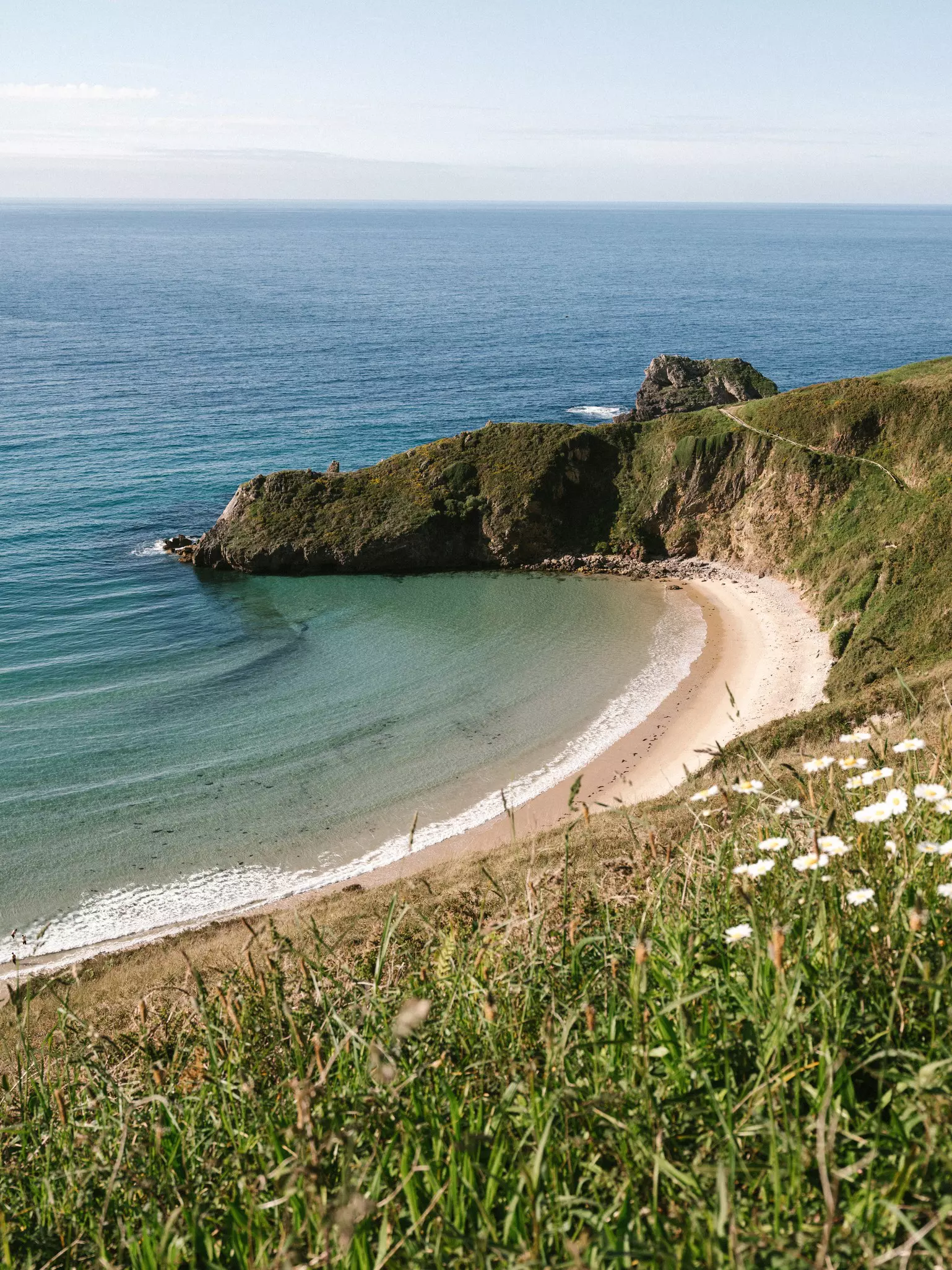 A shot from above of a crescent-shaped beach. Grassy hills descend to the beach.