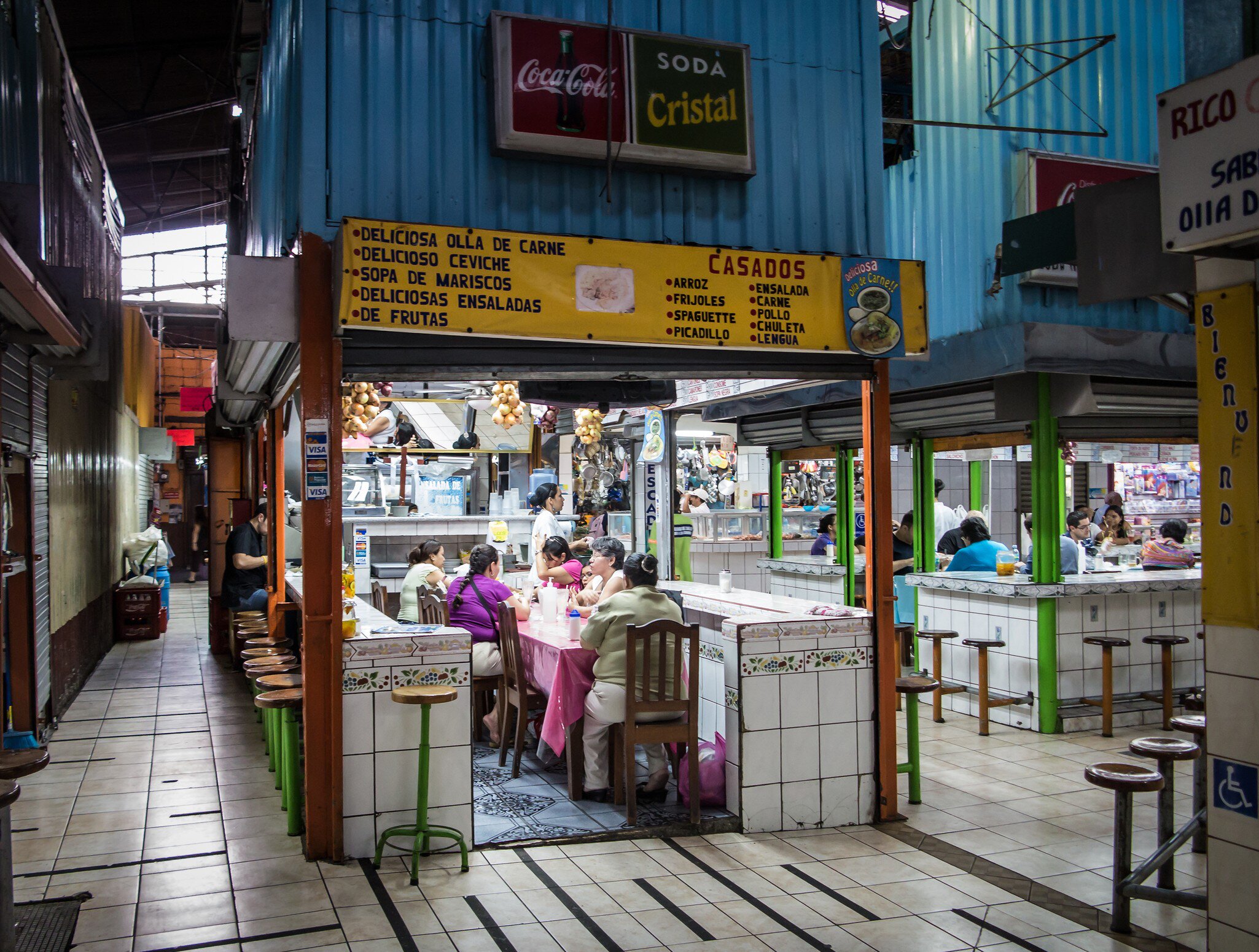 People dine at small food stalls in an enclosed market.