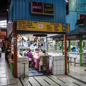 People dine at small food stalls in an enclosed market.