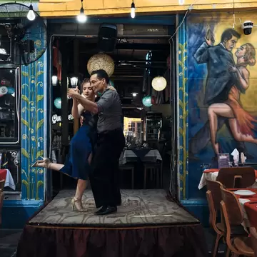 Two dancers performing the tango on a small stage in a restaurant. 