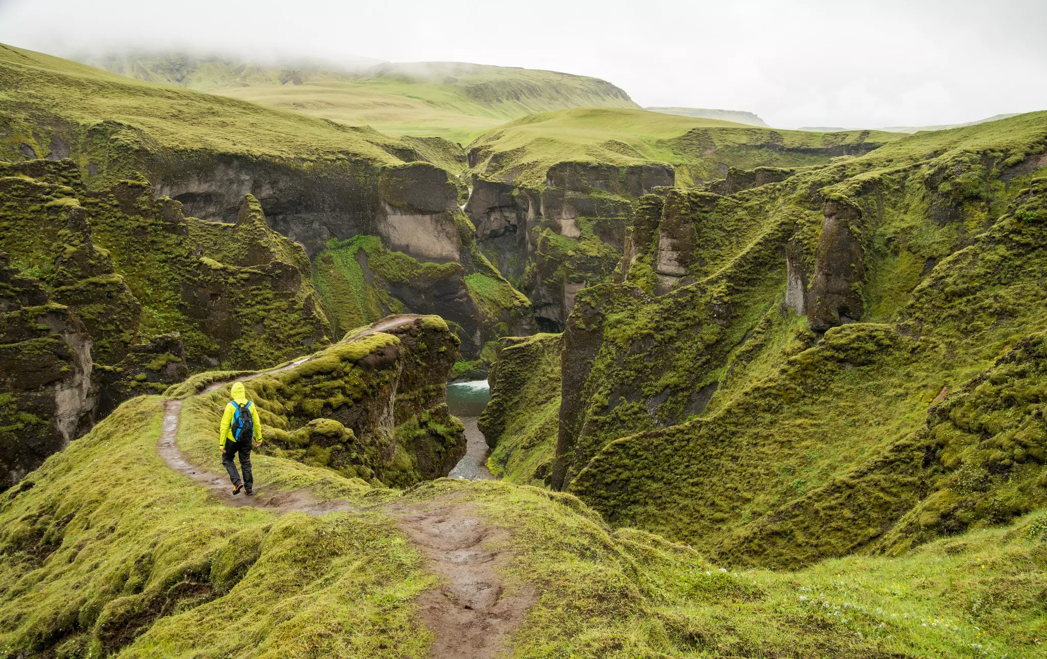 A hiker carrying a backpack follows a narrow trail that leads down towards a river canyon 