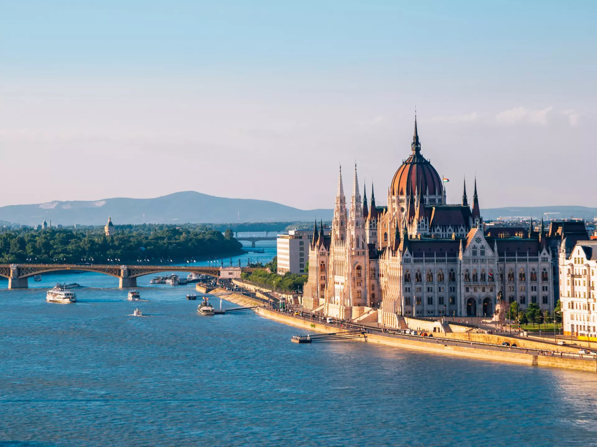 An ornate building by a bridge over a blue river with boats.