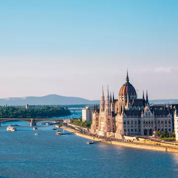 An ornate building by a bridge over a blue river with boats.