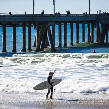 A surfer stands in the foam looking out at a rainbow on the horizon