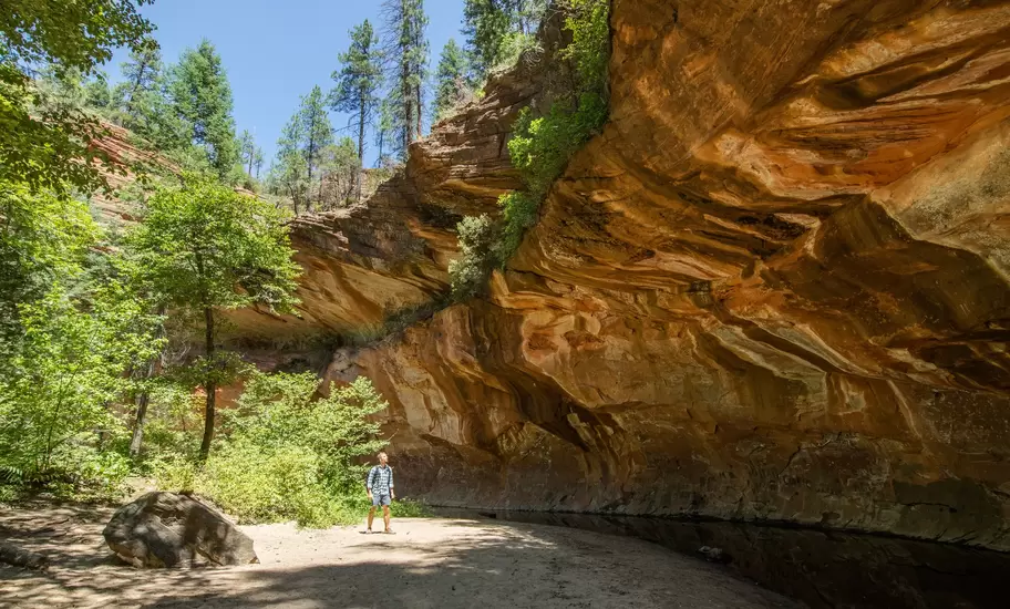 Man trekking through Oak Creek Canyon on the West Fork trail in Arizona, between Flagstaff and Sedona surrounded by beautiful red rock and lush green forest