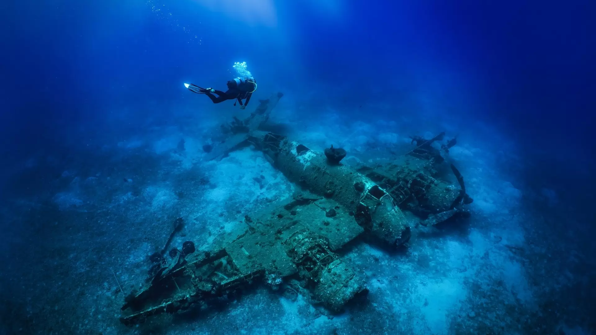 A scuba diver descending to a sunken world war two fighter propeller airplane at the seabed of the Aegean Sea, Naxos island, Greece