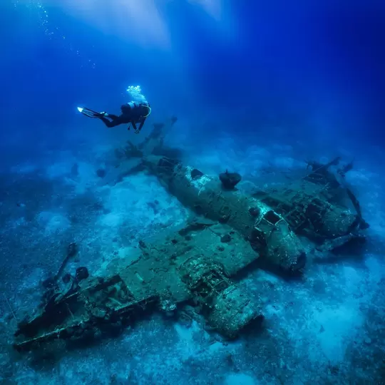 A scuba diver descending to a sunken world war two fighter propeller airplane at the seabed of the Aegean Sea, Naxos island, Greece