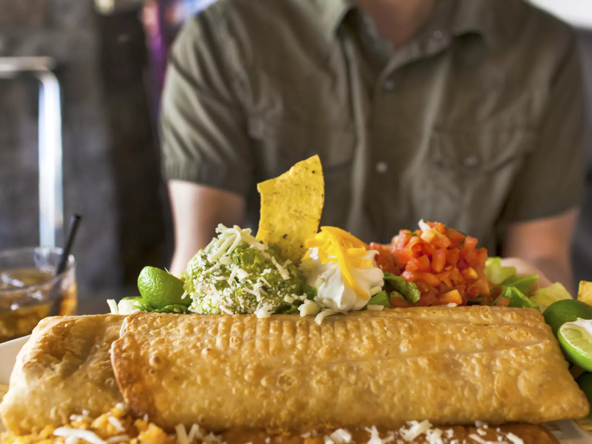 A man sitting at a Mexican food restaurant about to eat a giant chimichanga (fried burrito).
451158965
USA, Food and Drink, Tomato, Mexican Culture, Casual Clothing, L