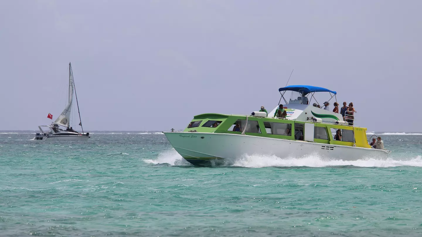A ferry boat glides through the water past a small sailboat.