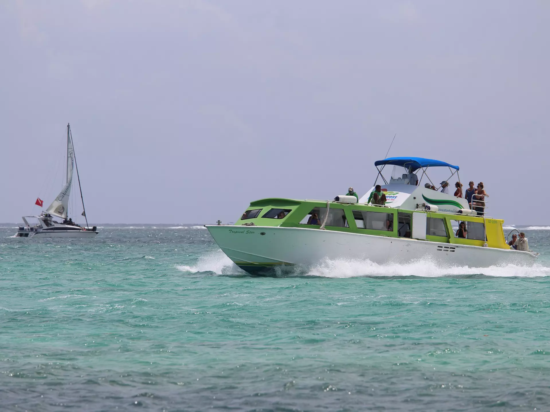 A ferry boat glides through the water past a small sailboat.