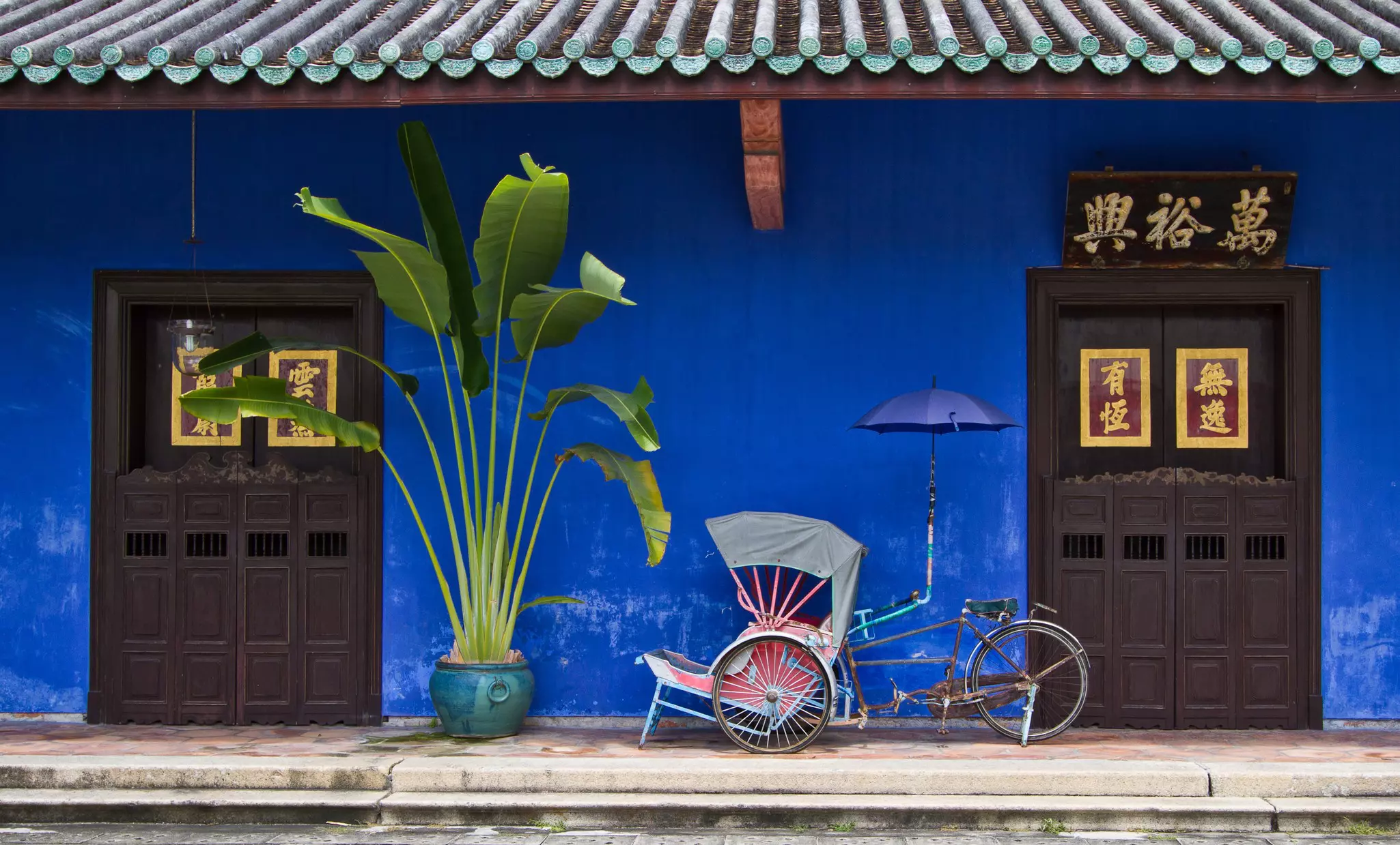 A rickshaw is parked in front of a house with a blue facade and tiled awning
