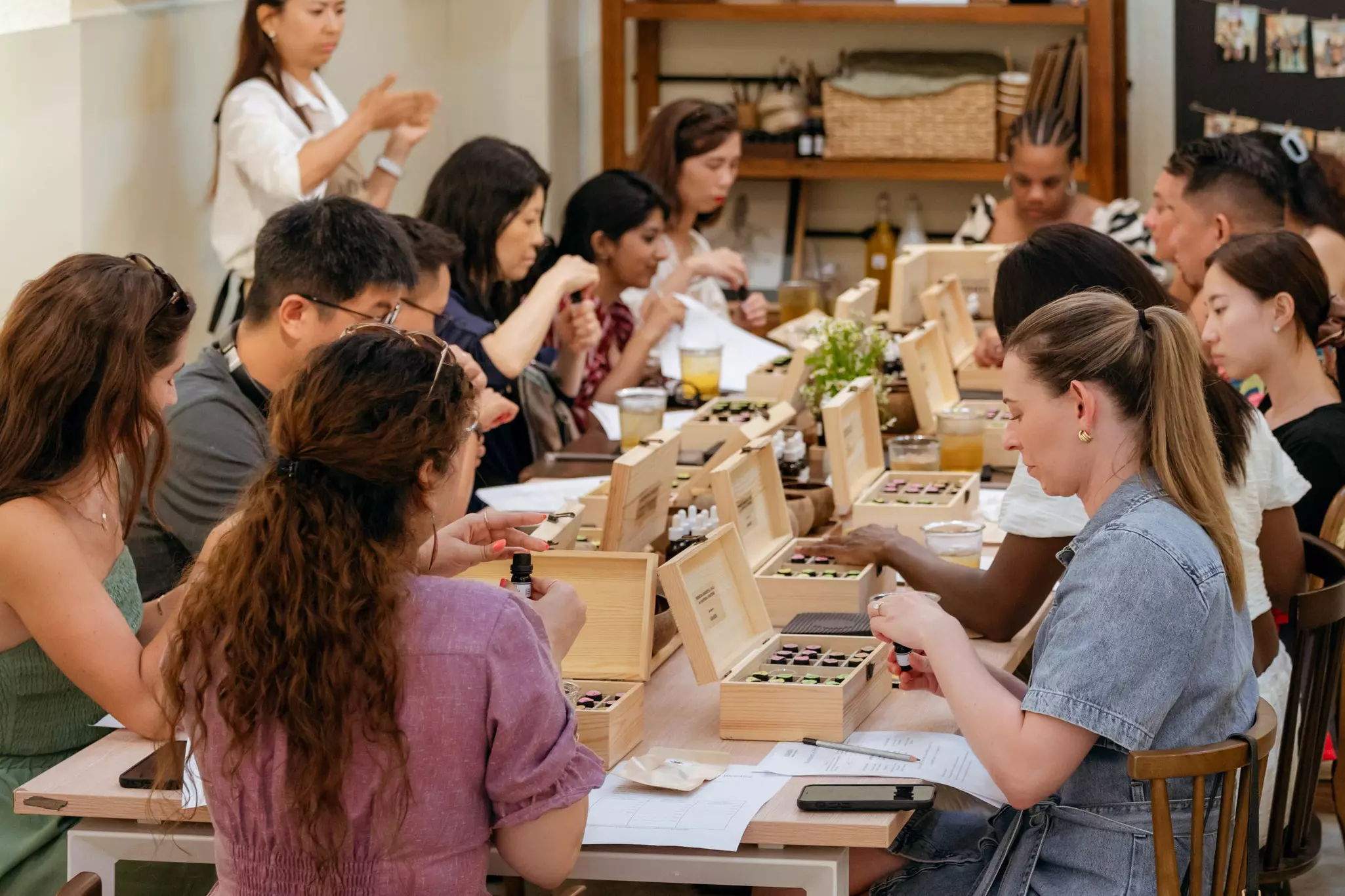People sitting around a rectangular table in front of wooden boxes that hold various small containers