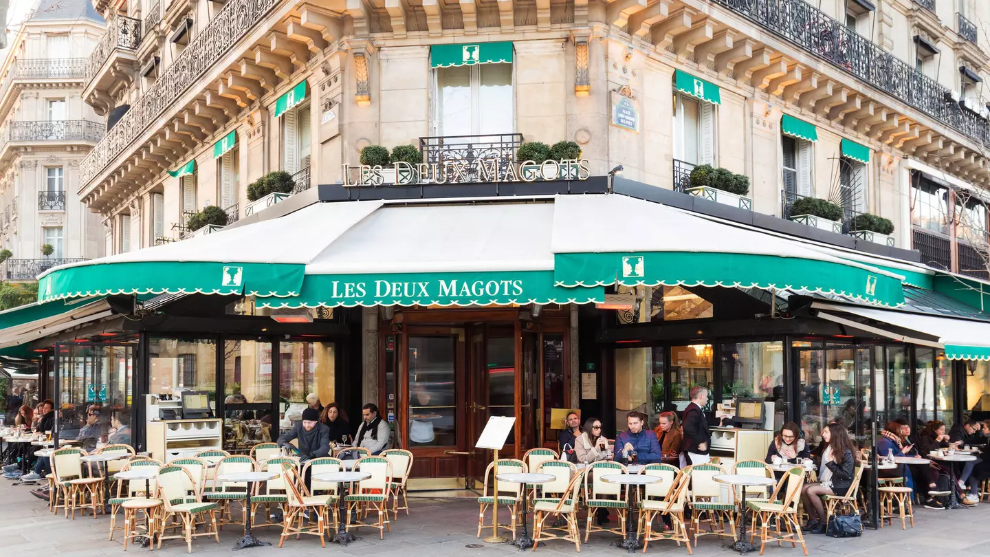 People gather at tables outside a traditional Parisian cafe