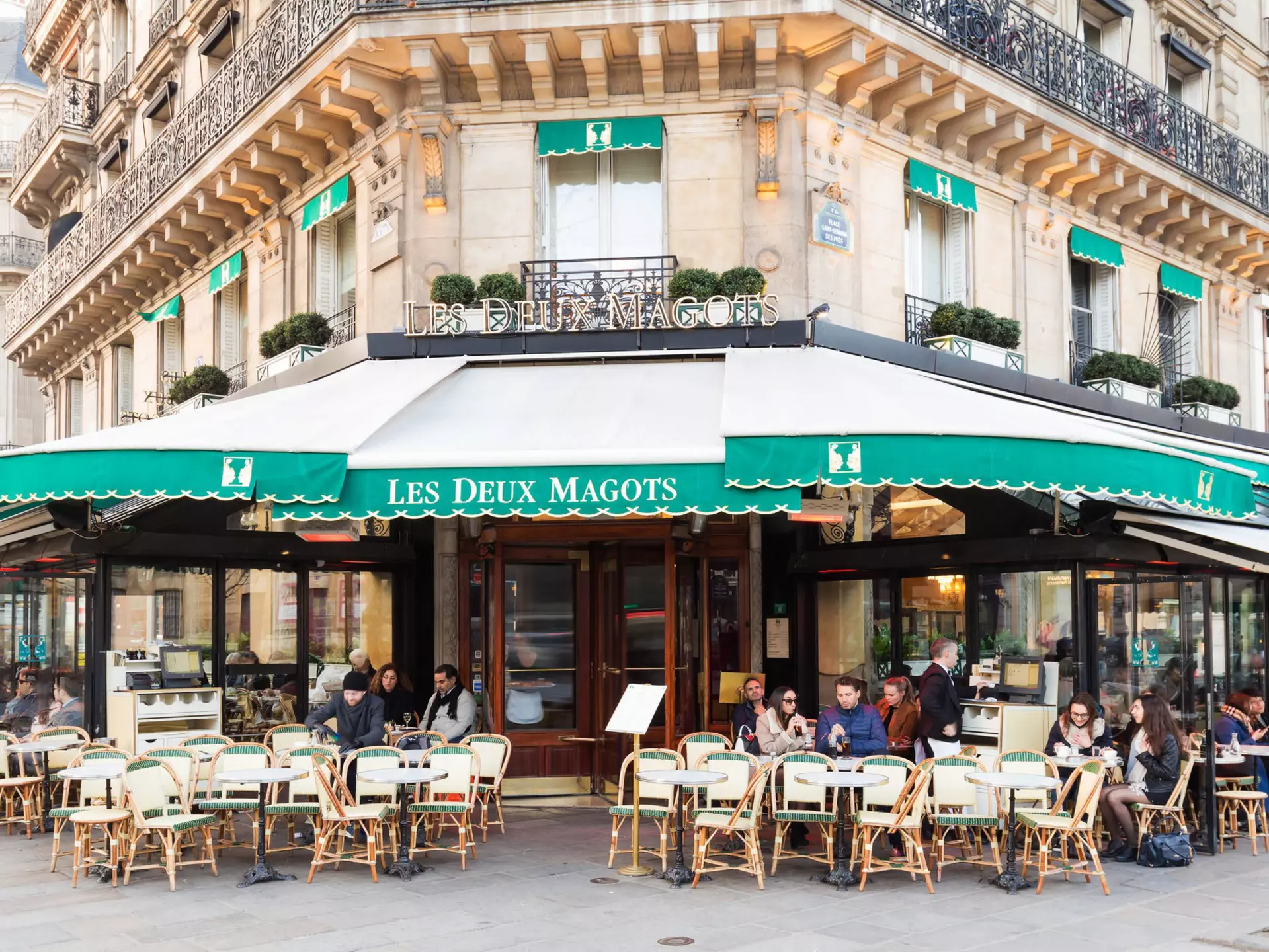 People gather at tables outside a traditional Parisian cafe