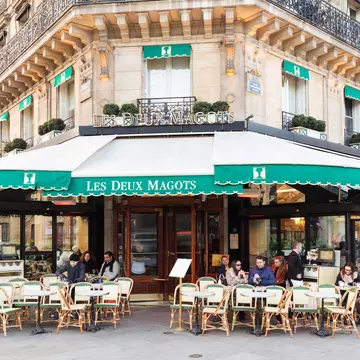 People gather at tables outside a traditional Parisian cafe