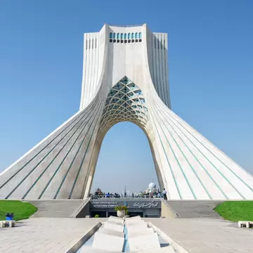 White marble Azadi Tower in Tehran with turquoise-tiled arch; sign reads Azadi Tower Artistic and Cultural Complex