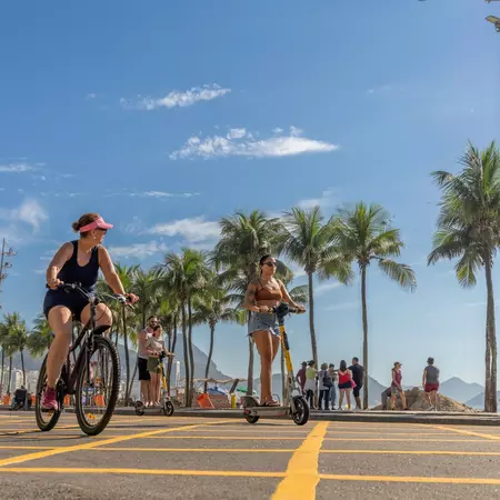  People riding on bicycle and electric scooter by the famous Copacabana Beach with morning sun, Rio de Janeiro, Brazil