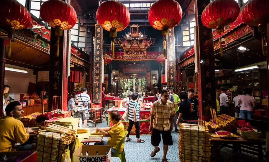 Worshippers and incense sellers beneath red lanterns in an ornate Chinese temple hall in Malaysia