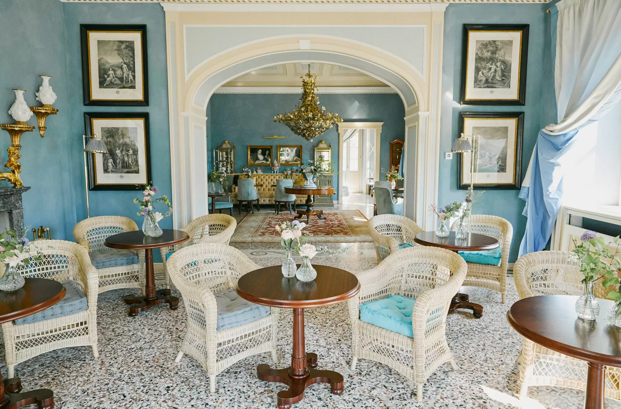 A sumputuously designed blue room with a central arch leading through to another salon dominated by a gold chandelier: Passalacqua boutique hotel, Lake Como, Italy