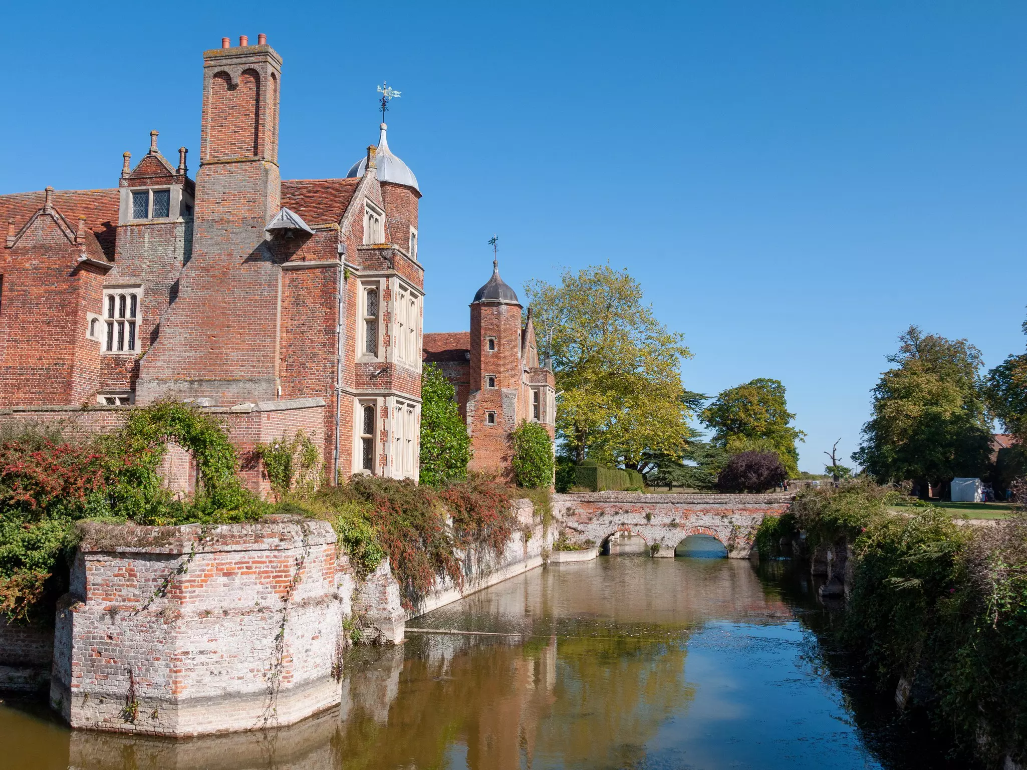 A red-brick Tudor manor house at the edge of a moat
