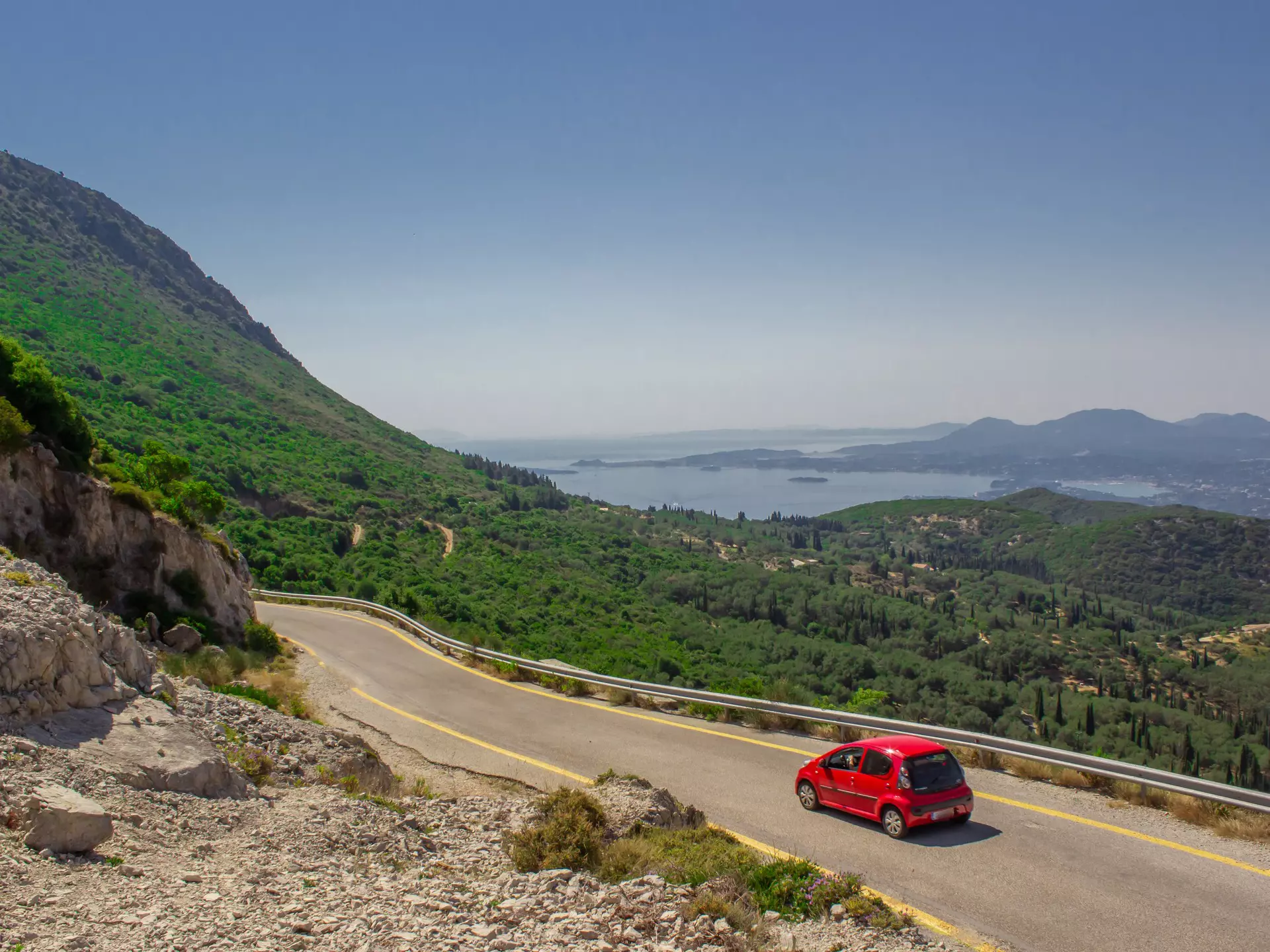 A small red car on the mountain road to the sea.